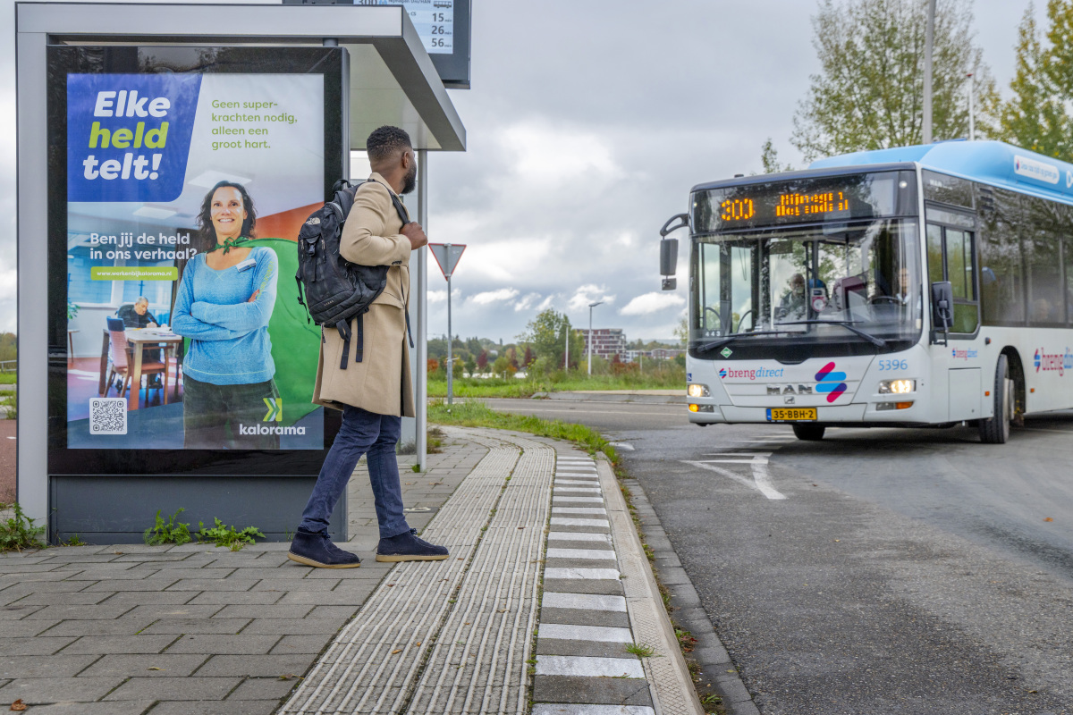 Reiziger wacht bij de bushalte op de bus, die er net aan komt rijden